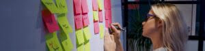 Project management agile methodology, concept. A young blonde woman in glasses, gluing colored sticky notes on a magnetic Board.